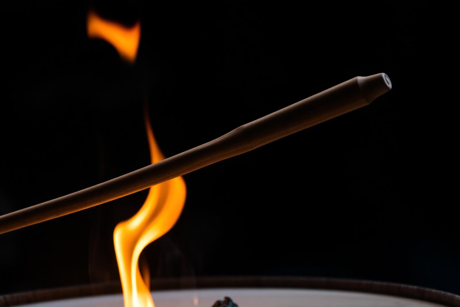 A wooden drumstick being passed through a controlled flame for fire-tempering